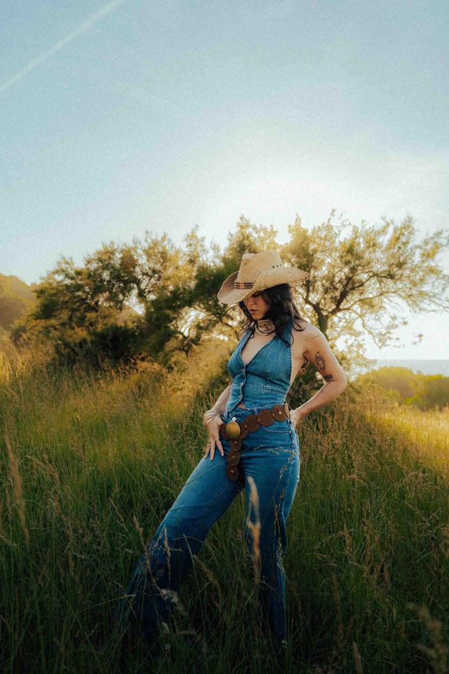 Portrait de mode dans un champ au coucher du soleil, chapeau et lumière dorée